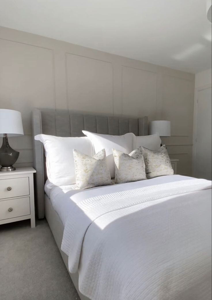 Bright bedroom with white bedding, decorative pillows, and matching nightstands with lamps.