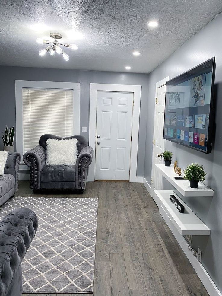 Modern living room with gray sofas, fluffy pillows, patterned rug, and wall-mounted TV.